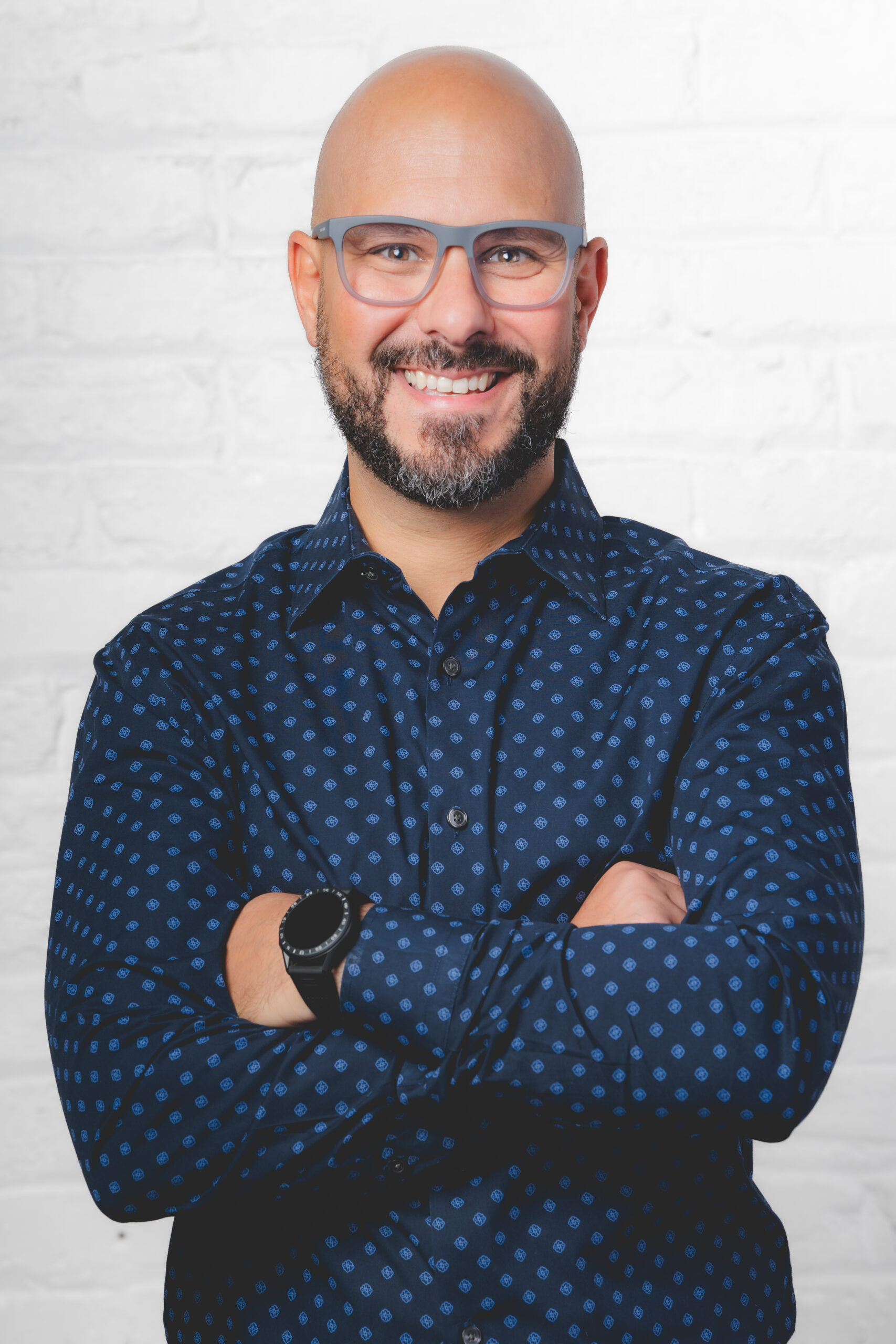 Smiling man with glasses and beard in a patterned shirt.